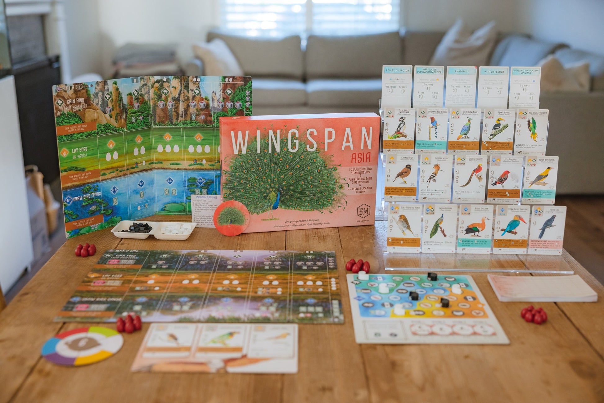 Wingspan Asia - Wingspan Asia bird-themed board game with colorful cards, bird tokens, and illustrated game board on wooden table.