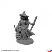 Cynthia the Wicked Witch - Gray resin miniature of a witch wearing a wide-brimmed hat and long dress, holding a staff with a carved jack-o'-lantern at.