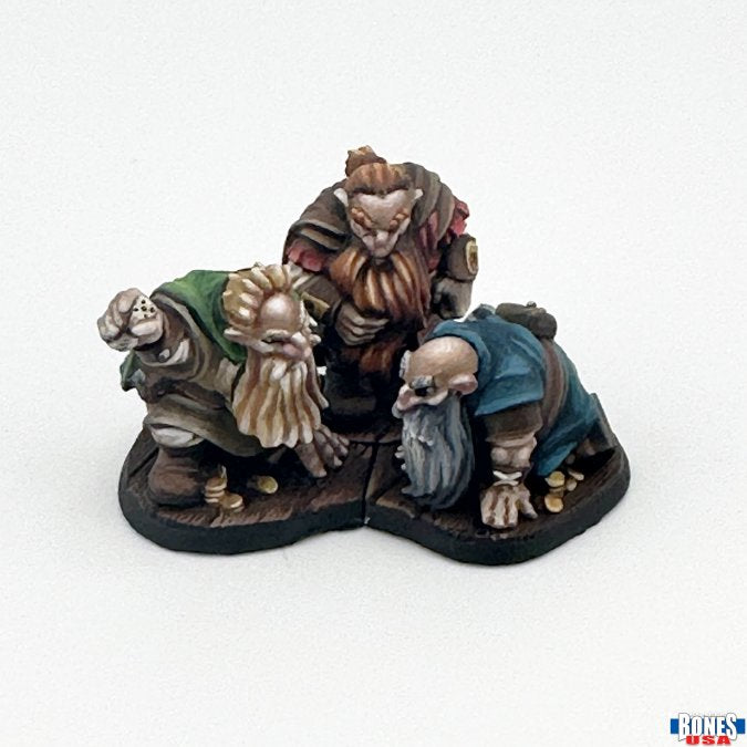 Townsfolk: Gambling Dwarves (3) - Three detailed dwarf figurines with distinct beards and clothing, posed as if gambling, on a dark base.