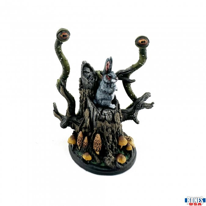 Wolf in Sheep's Clothing - Dark gray wolf figurine emerging from a twisted black tree stump with orange mushrooms and two green eye stalks on an oval.