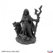 Isidora, Witch - Dark gray resin miniature of a cloaked witch holding a twisted staff, standing on a textured base with skulls and stones.