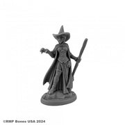 Wild West Oz - Wicked Witch - Gray resin miniature of a witch in a flowing dress and cape, wearing a pointed hat and holding a broomstick upright.