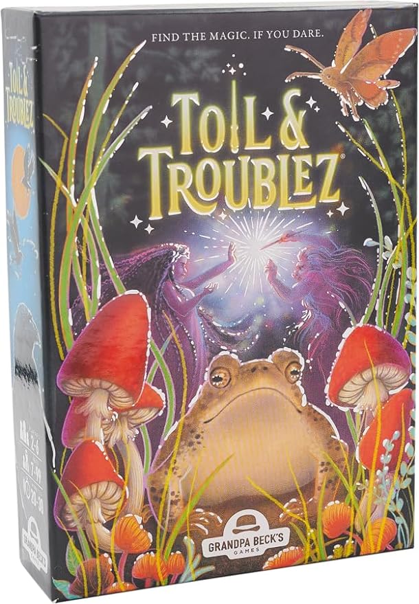 Toil & Troublez - Colorful Toil & Troublez card game box featuring a golden frog, red mushrooms, and a glowing magical aura with a fairy.