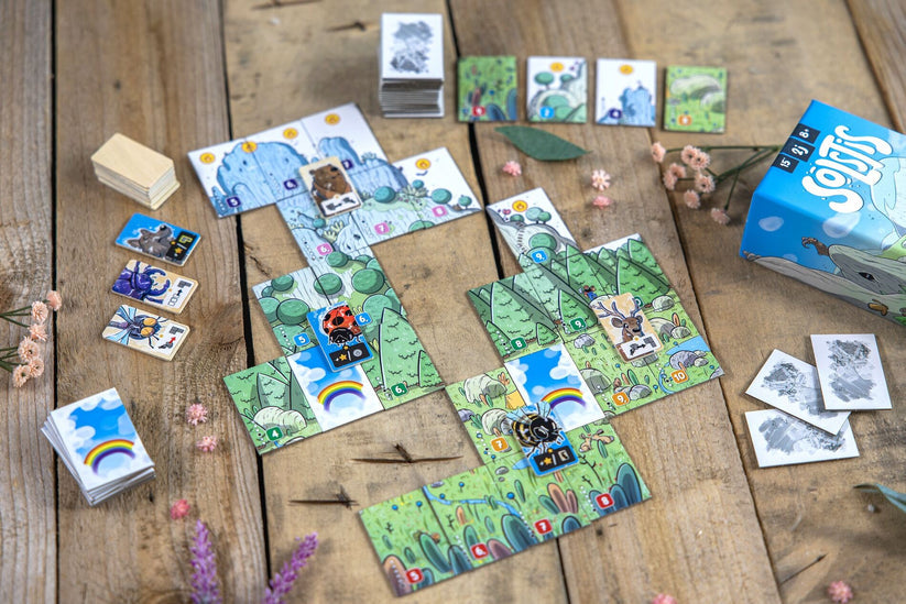 Solstis - Board game setup with colorful illustrated square tiles featuring nature motifs, small wooden animal tokens, cards with.