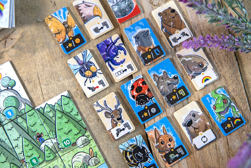 Solstis - Wooden rectangular game tiles with colorful animal illustrations and numeric values, arranged on a wooden surface next to.