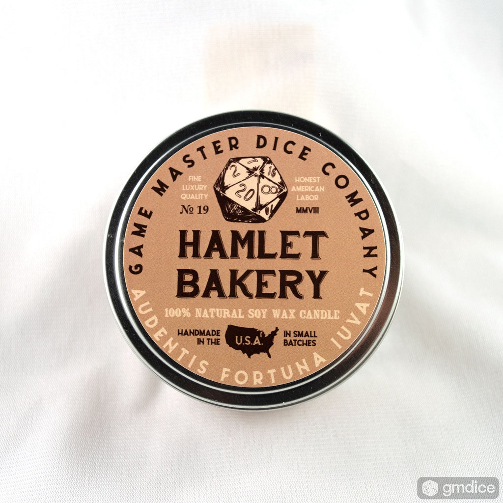Hamlet Bakery Gaming Candle - Round tin candle with beige label featuring black lettering and a dice illustration, branded Hamlet Bakery by Game Master.