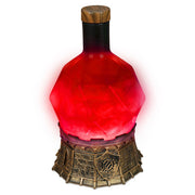 Enhance: Tabletop Potion Light: Red - Red faceted glass potion-shaped light with black neck and wooden stopper on ornate bronze base.