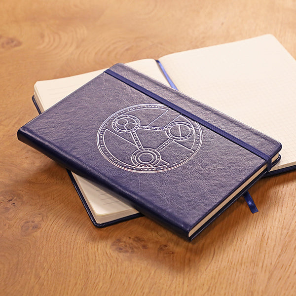 Critical Role Mighty Nein Cobalt Journal - Navy blue hardcover journal with embossed circular arcane design and elastic band closure, lying on open cream pages.