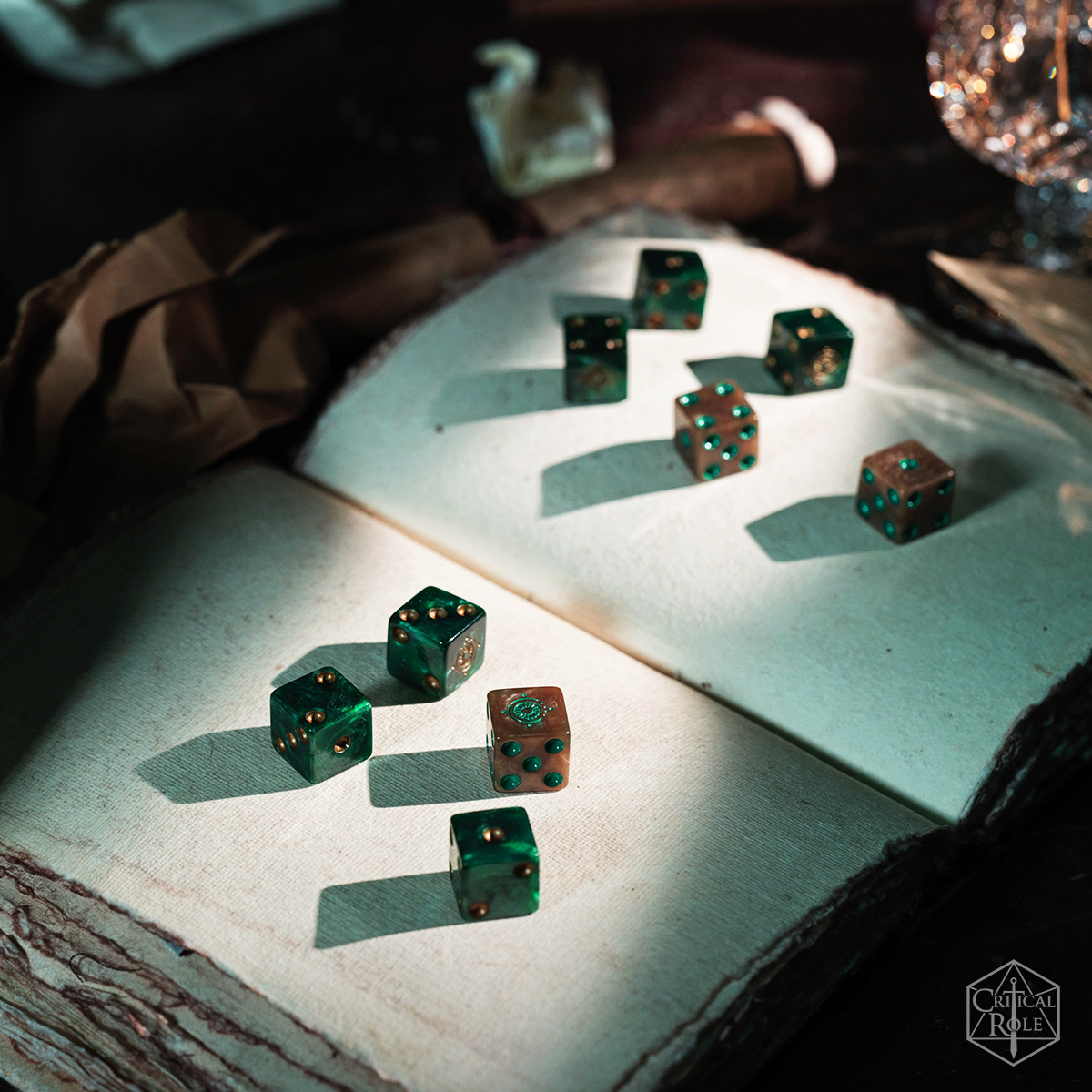 Candela Obscura Official Dice Set - Set of translucent green polyhedral dice with gold numbering, displayed on an open, textured book page.