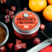 Dragon's Blood Gaming Candle - Red glass jar candle with orange and black label reading "Dragon's Blood," surrounded by red and black gaming dice and an.