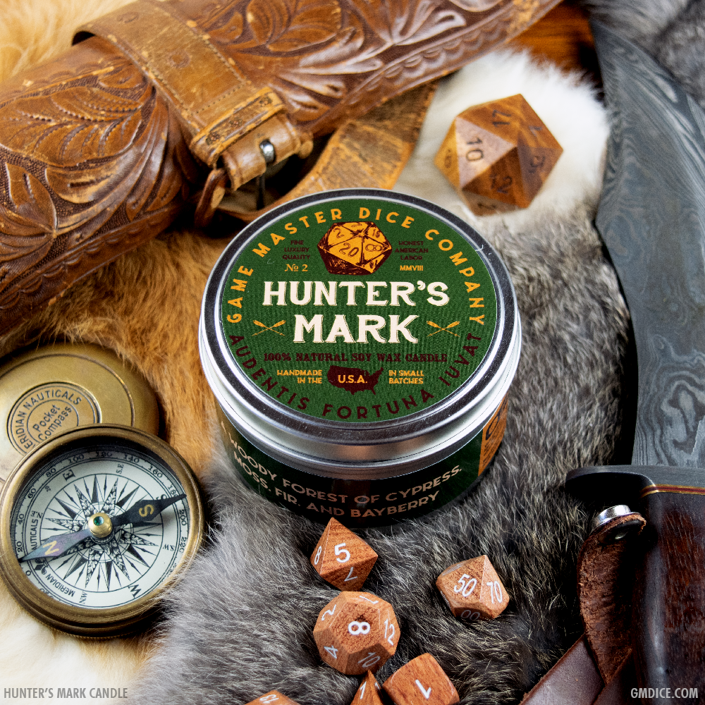 Hunter's Mark Gaming Candle - Round green metal tin candle labeled "Hunter's Mark" with orange and white text, surrounded by wooden polyhedral dice, a.