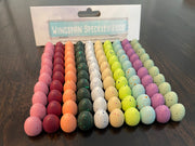 100 Speckled Eggs for Wingspan - Colorful speckled game eggs in rows of pink, green, black, white, yellow, purple, and light blue on a wooden surface with.
