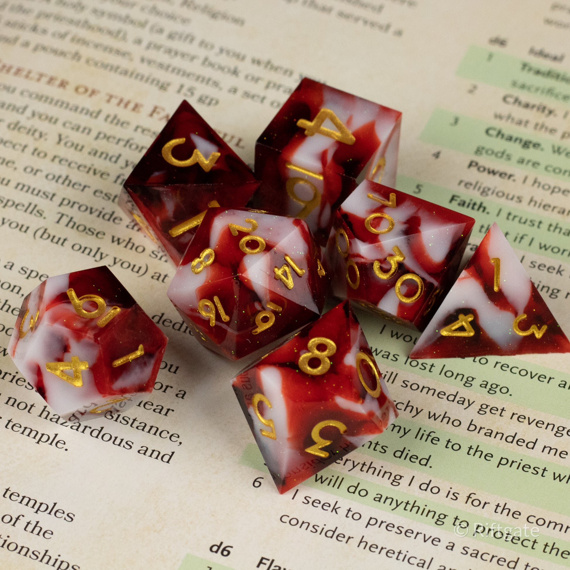 Blood and Snow Dice Set - Red and white marbled seven-piece sharp-edged dice set with gold numbers on book pages.