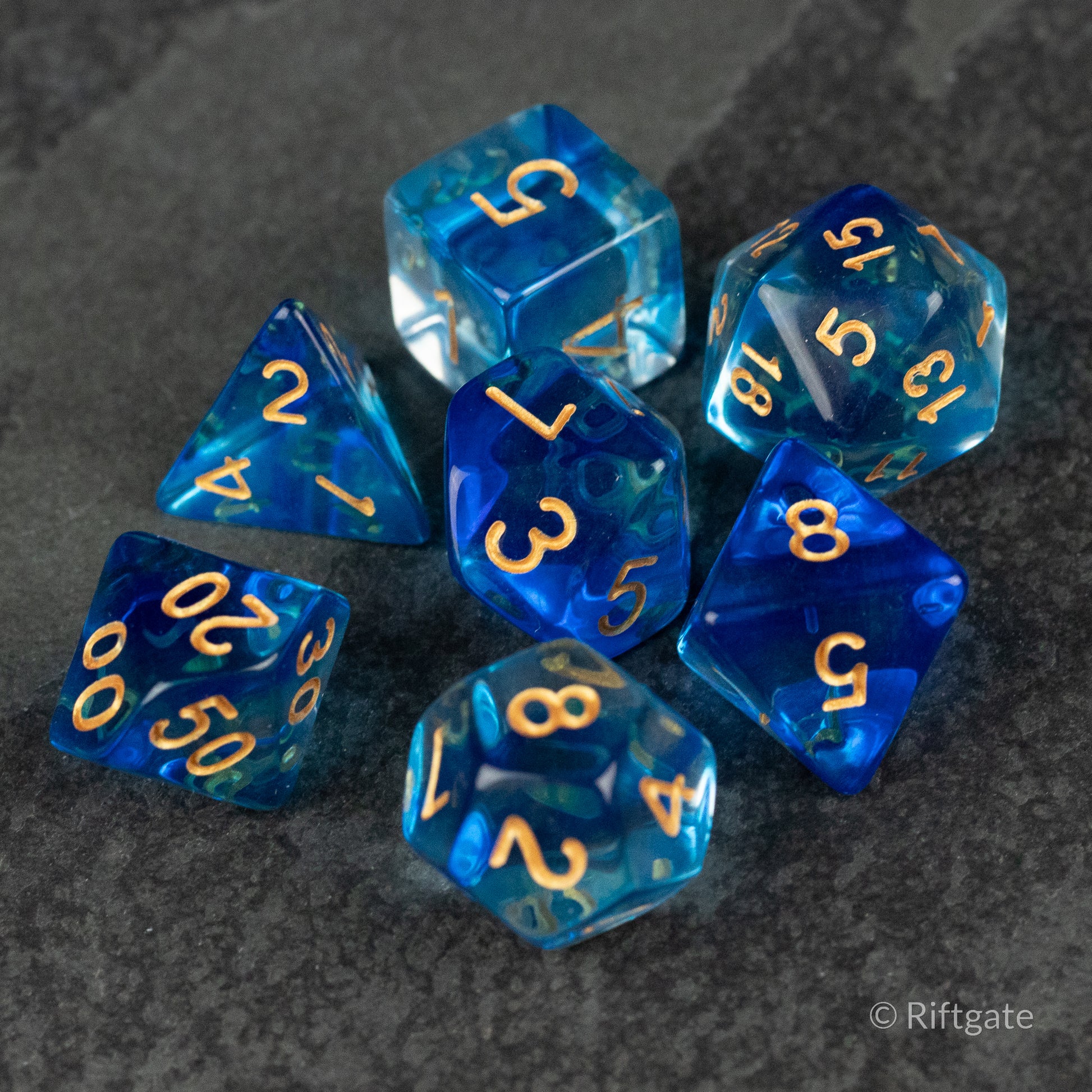 Ethereal Mist Dice Set - Set of seven translucent blue polyhedral dice with gold numbers, including d20, d12, d10, d8, d6, and d4, displayed on a.
