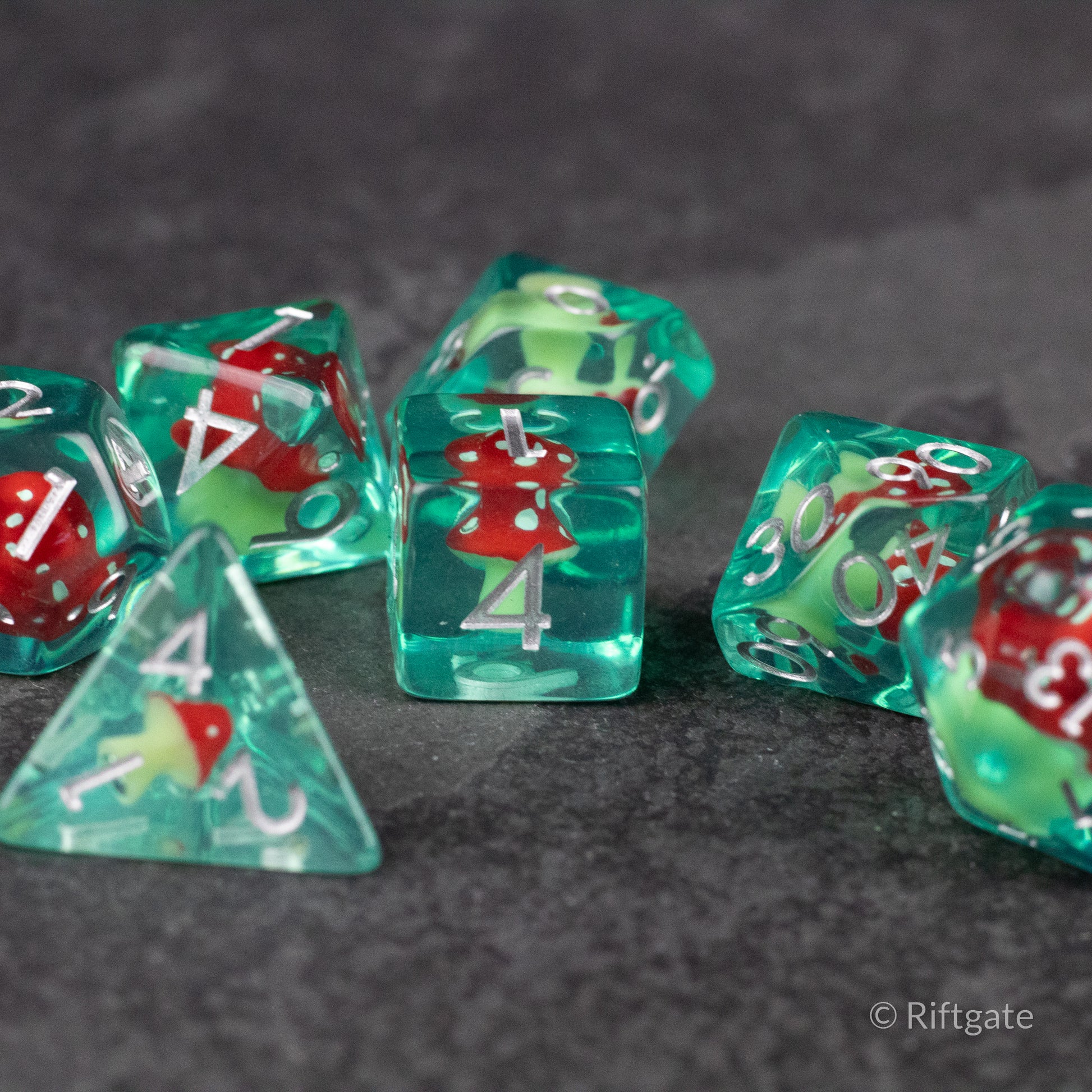 Red + Green Resin Mushroom Dice Set - Translucent green resin dice set with red mushroom inclusions and white numbering on gray surface.