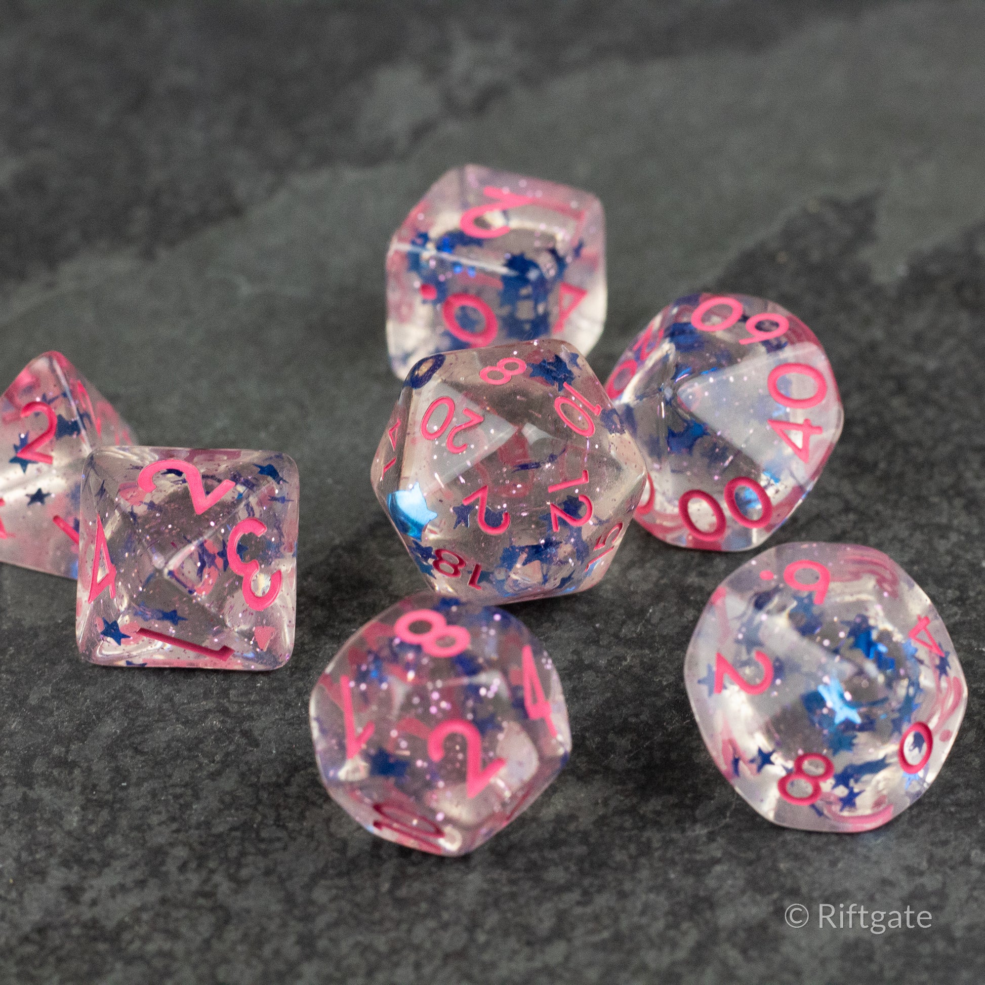 Blue Star Pink Glitter Dice - Set of translucent polyhedral dice with blue star inclusions and pink glitter, pink numbers visible on each face.