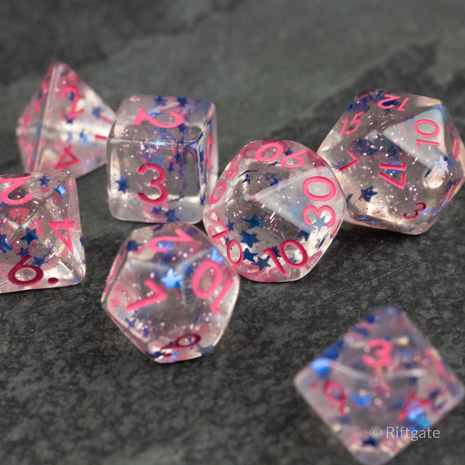 Blue Star Pink Glitter Dice - Set of transparent pink glittered polyhedral dice with bright blue star accents and pink numbers on dark surface.