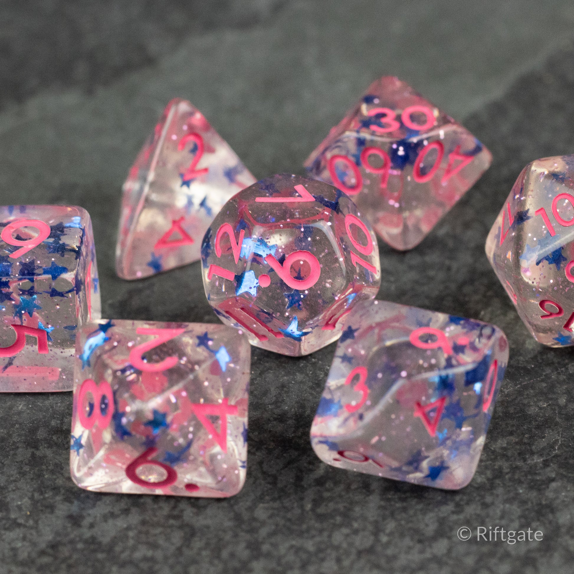 Blue Star Pink Glitter Dice - Clear polyhedral dice set with pink glitter, blue star inclusions, and pink numbers.