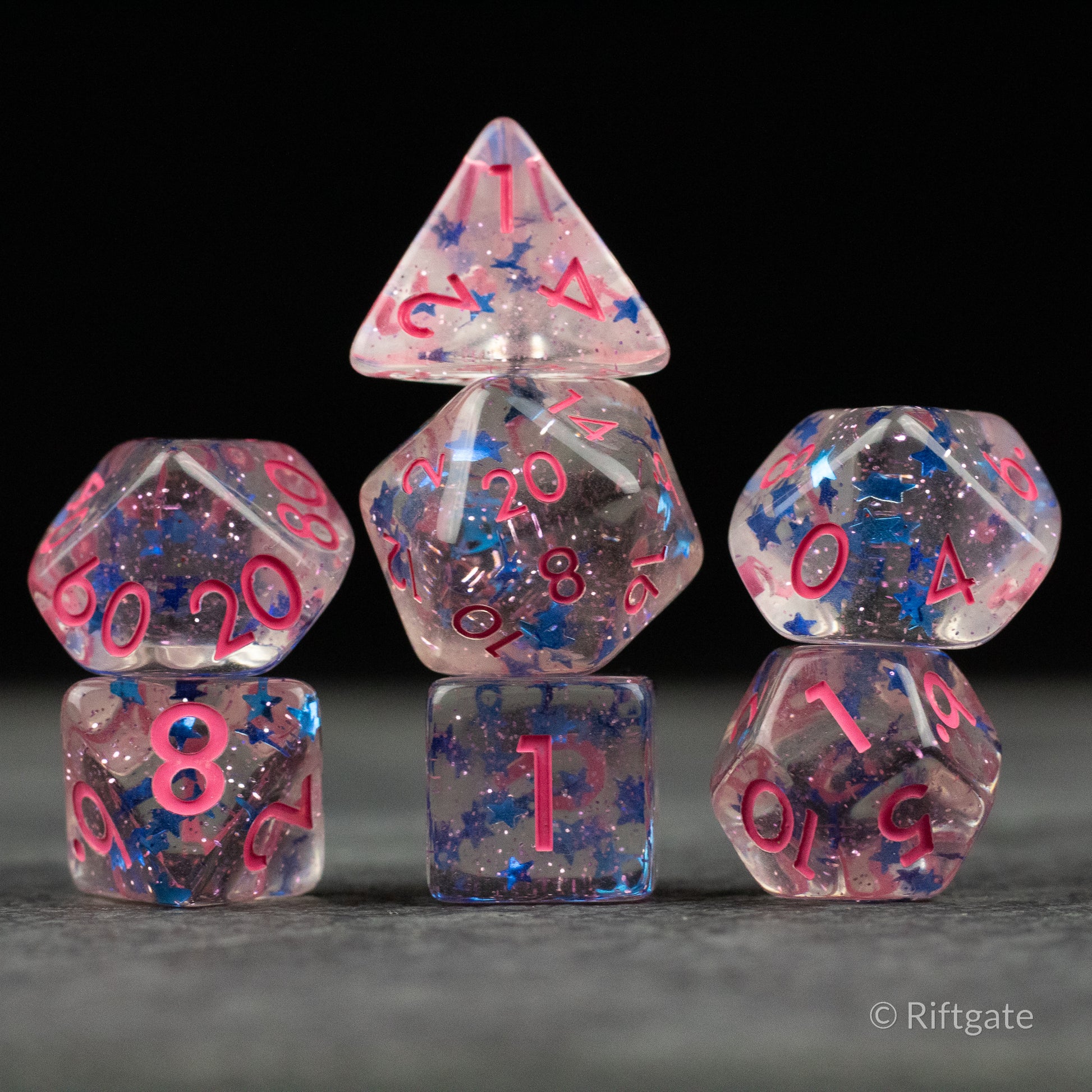 Blue Star Pink Glitter Dice - Set of seven translucent polyhedral dice with pink glitter and blue star inclusions, featuring bright pink numbers.