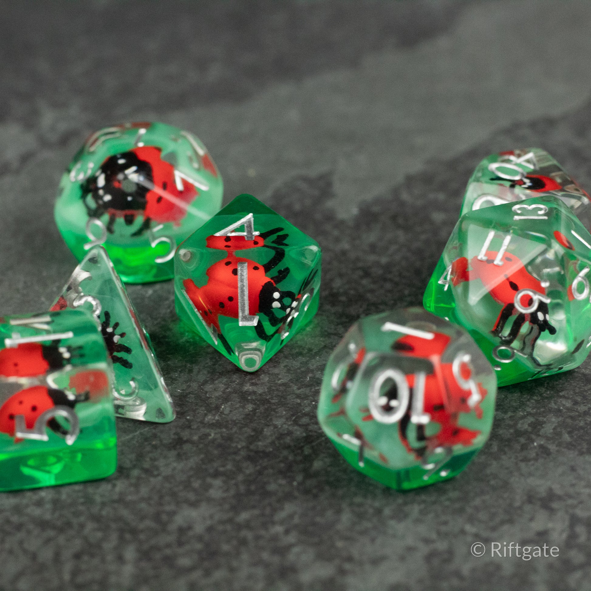 Ladybug Dice Set - Type 2 - Set of translucent green polyhedral dice with embedded red and black ladybug figures on a dark textured surface.