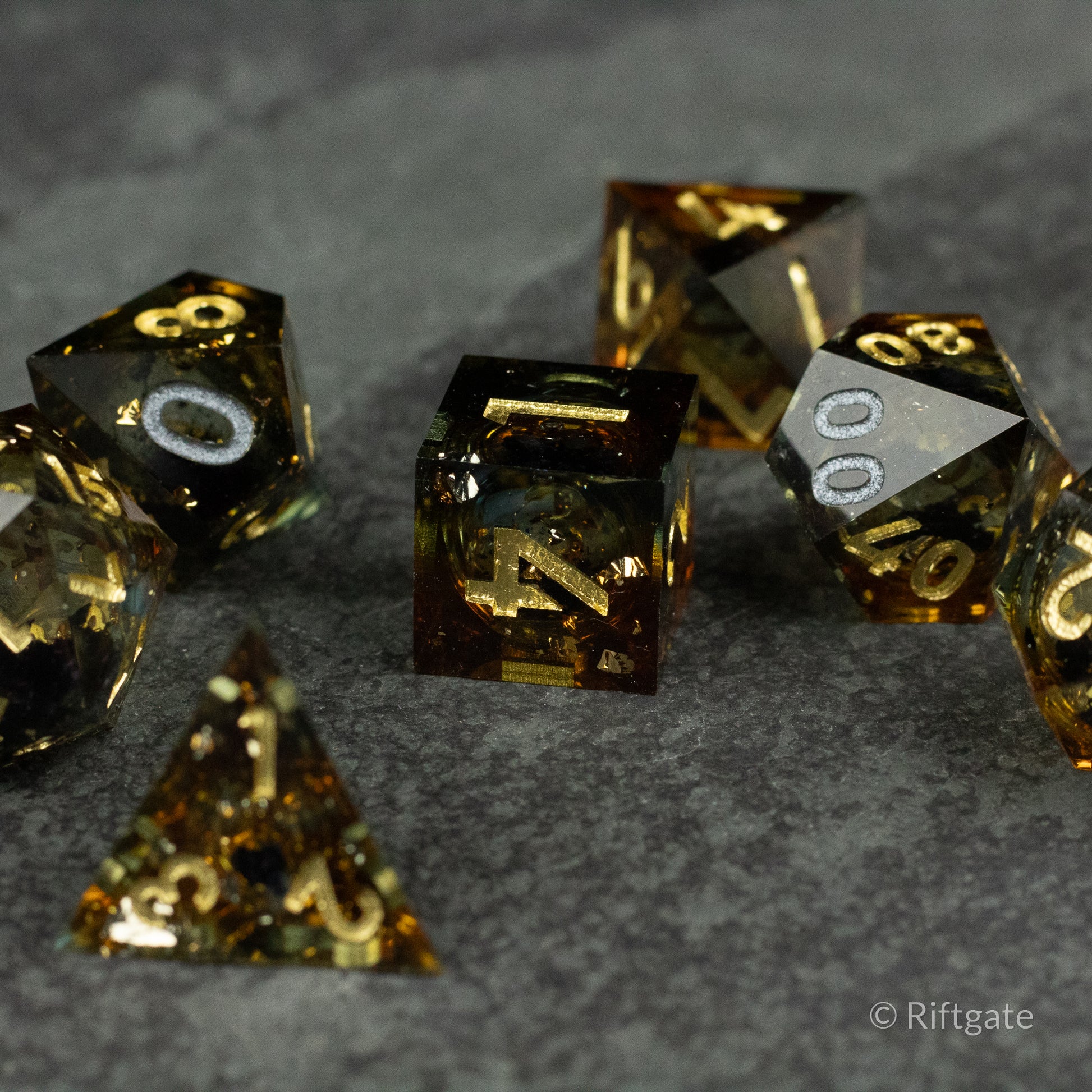 Ambershadow Dice Set - Set of translucent amber and black polyhedral dice with gold numbering on a dark textured surface.