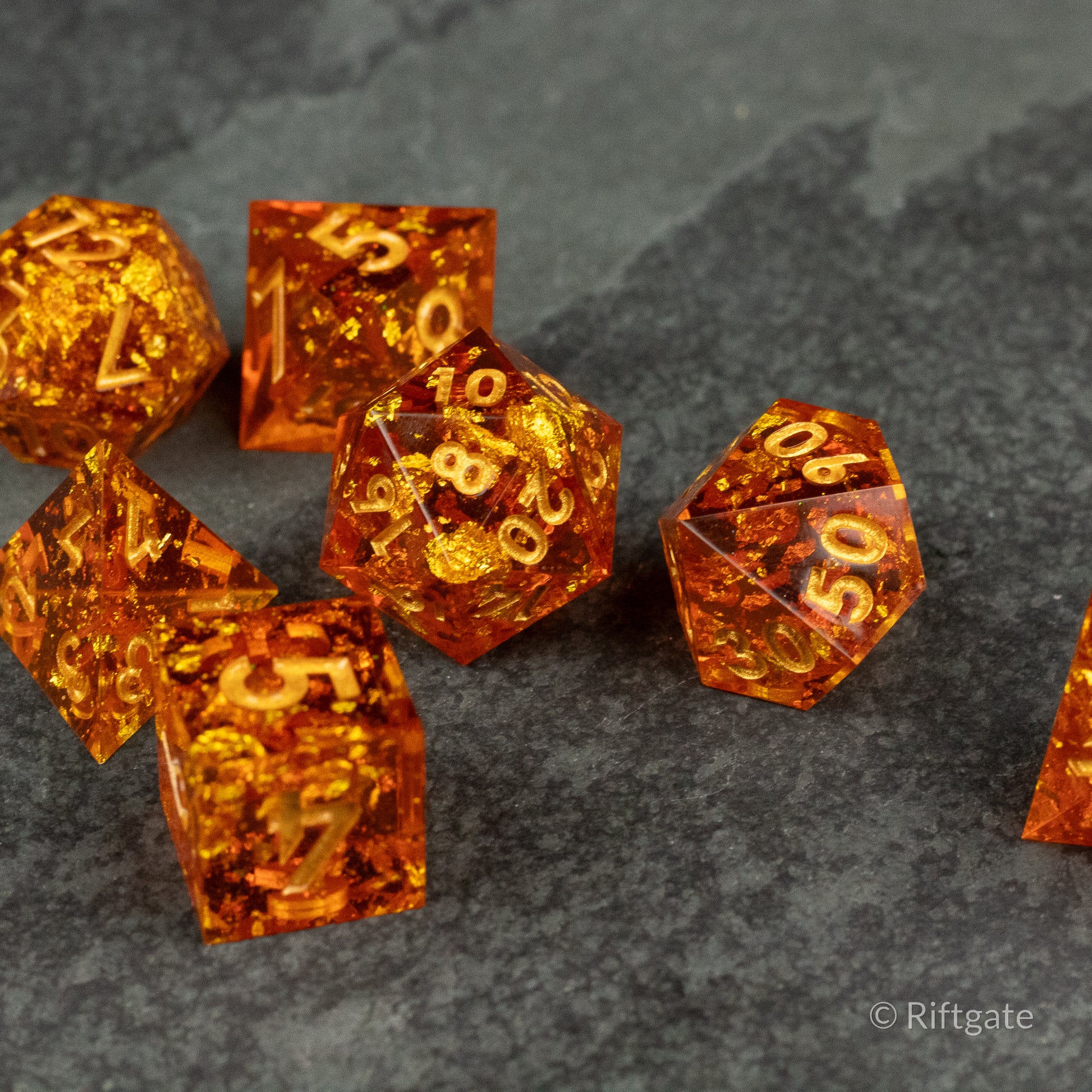 Sunforged Dice Set - Translucent amber-orange polyhedral dice set with sharp edges and gold numbering on a gray stone surface.