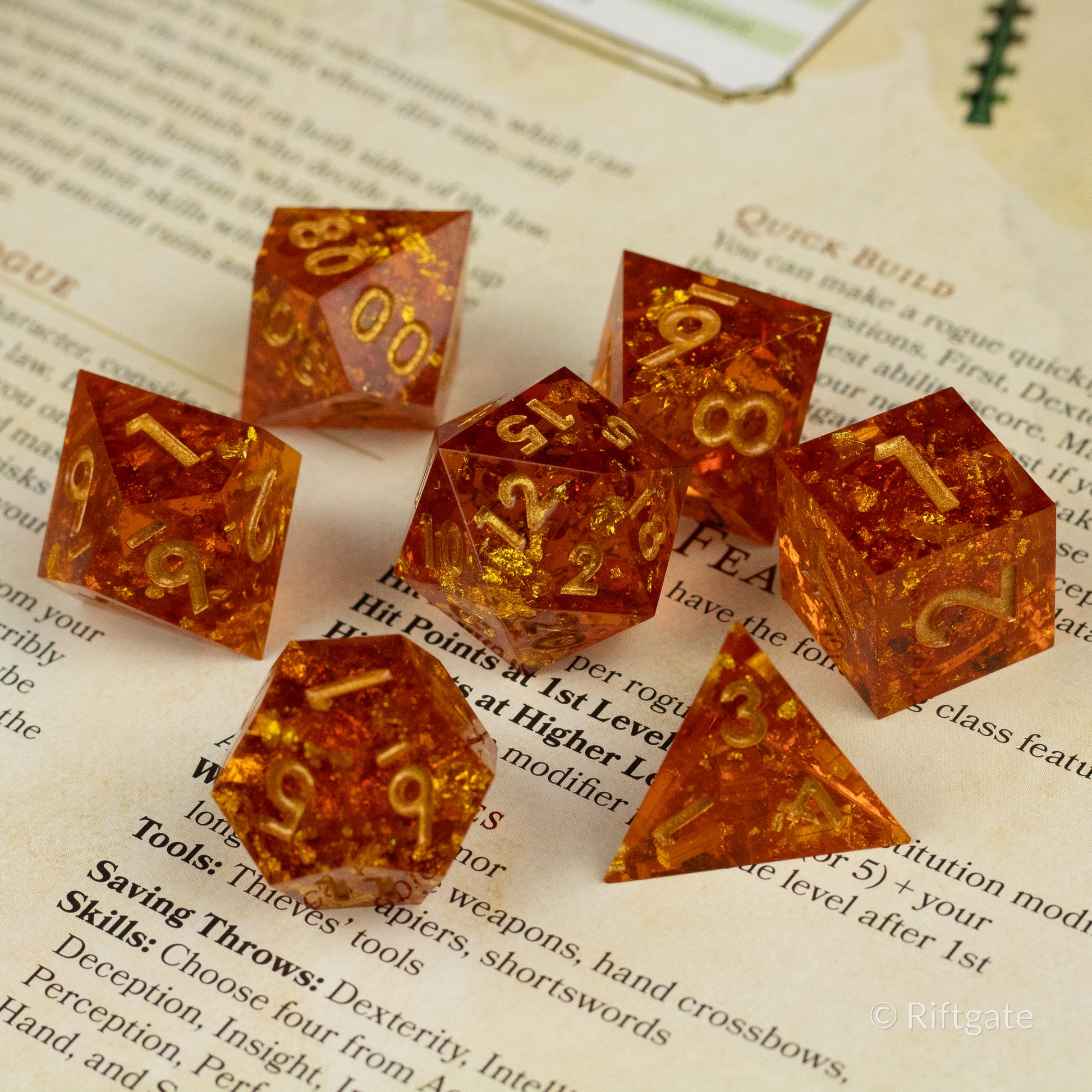 Sunforged Dice Set - Seven amber-orange translucent polyhedral dice with gold numbers, featuring sharp edges, arranged on a book page.