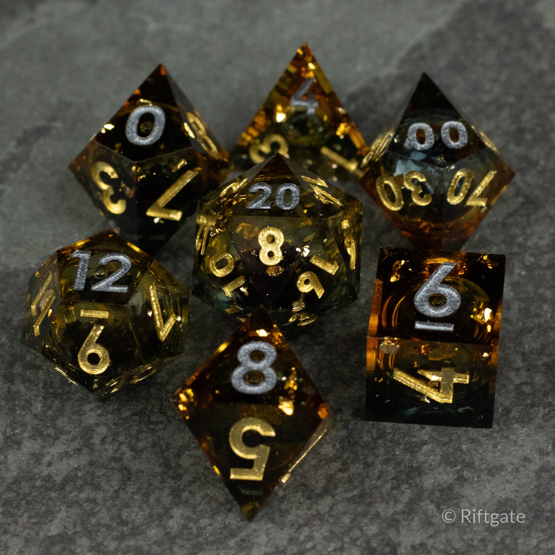 Ambershadow Dice Set - Seven amber and black translucent polyhedral dice with gold numbers on a dark gray surface.