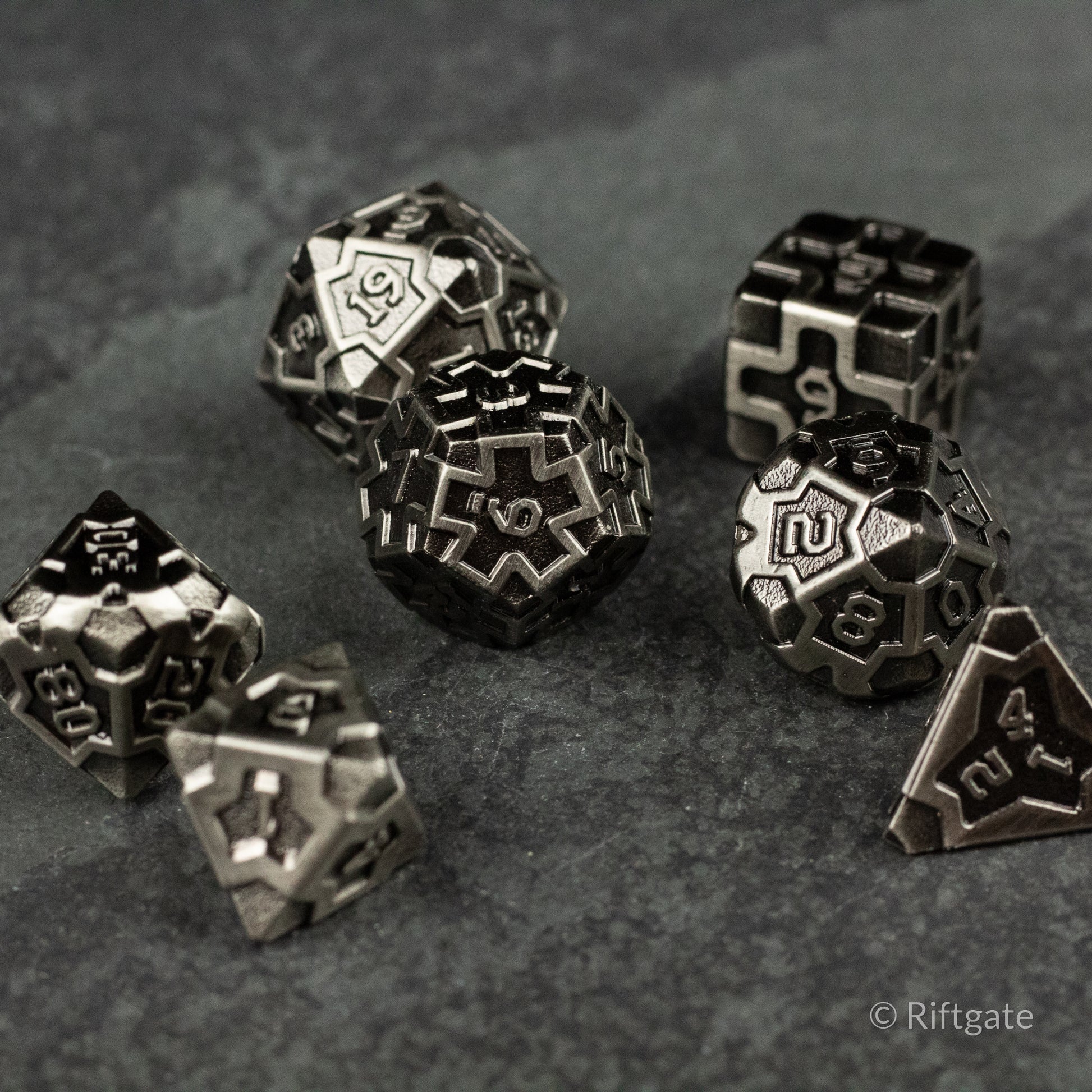Iron Crusader - Set of silver metallic polyhedral dice with intricate engraved numbers and geometric patterns on a dark textured surface.