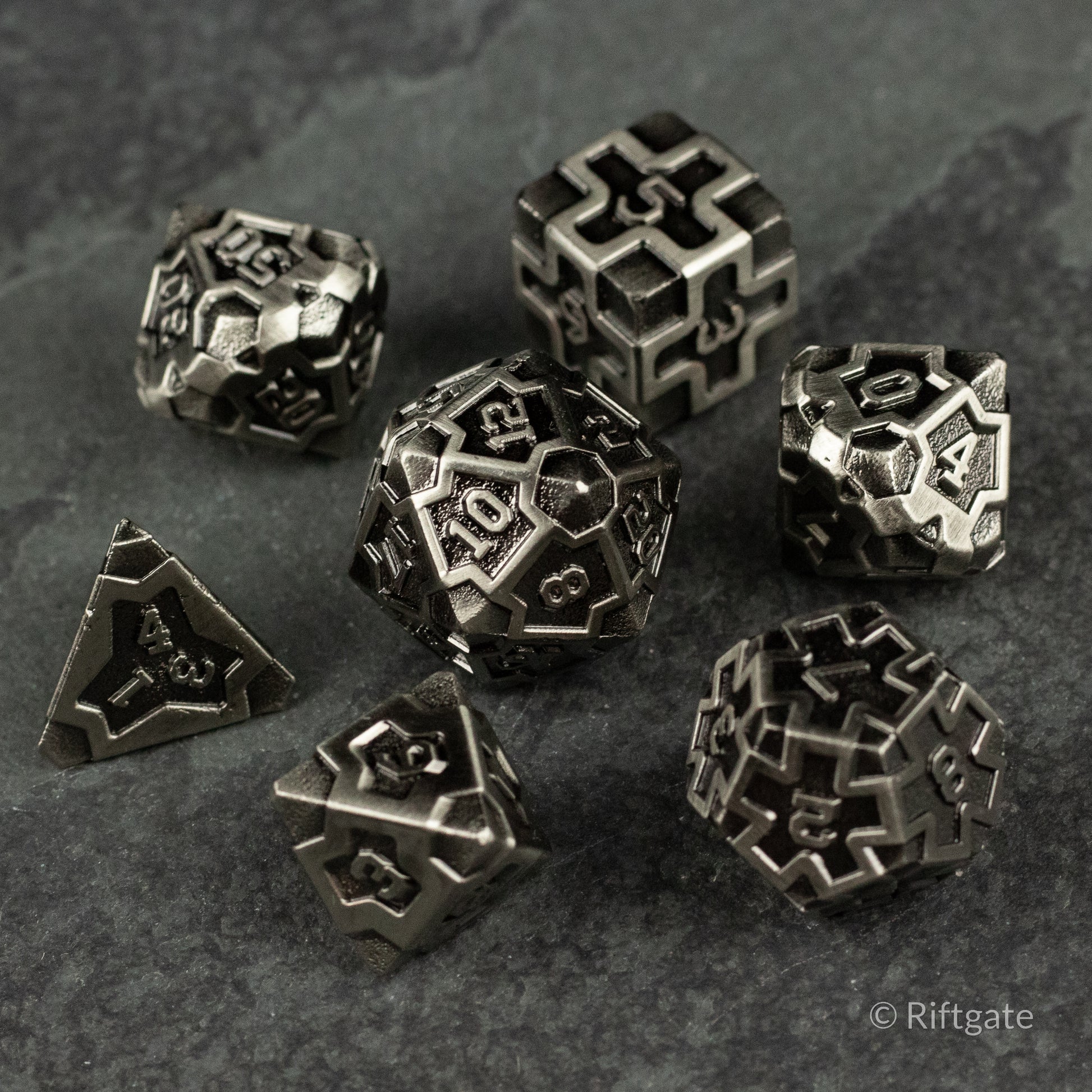 Iron Crusader - Set of seven metallic dice with intricate geometric cutouts and dark silver finish on a textured gray surface.