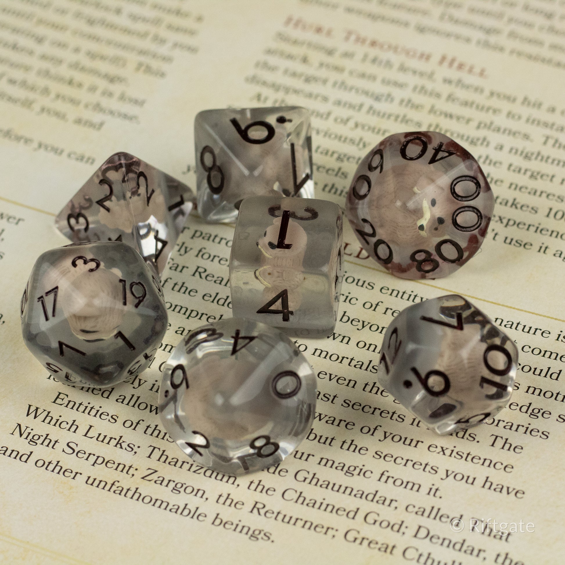 Scruffy Dog Dice - Set of seven translucent gray polyhedral dice with bold black numbers on an open book background.