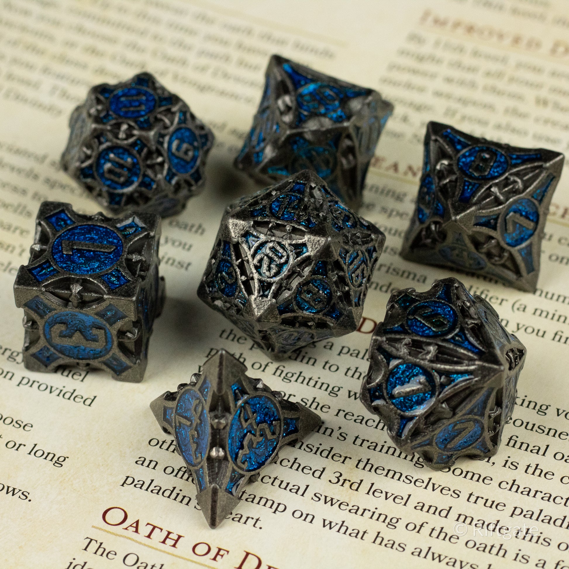 Gray Empyrean Artifact Dice Set - Set of seven gray metal dice with intricate blue enamel designs and numbers, various polyhedral shapes.