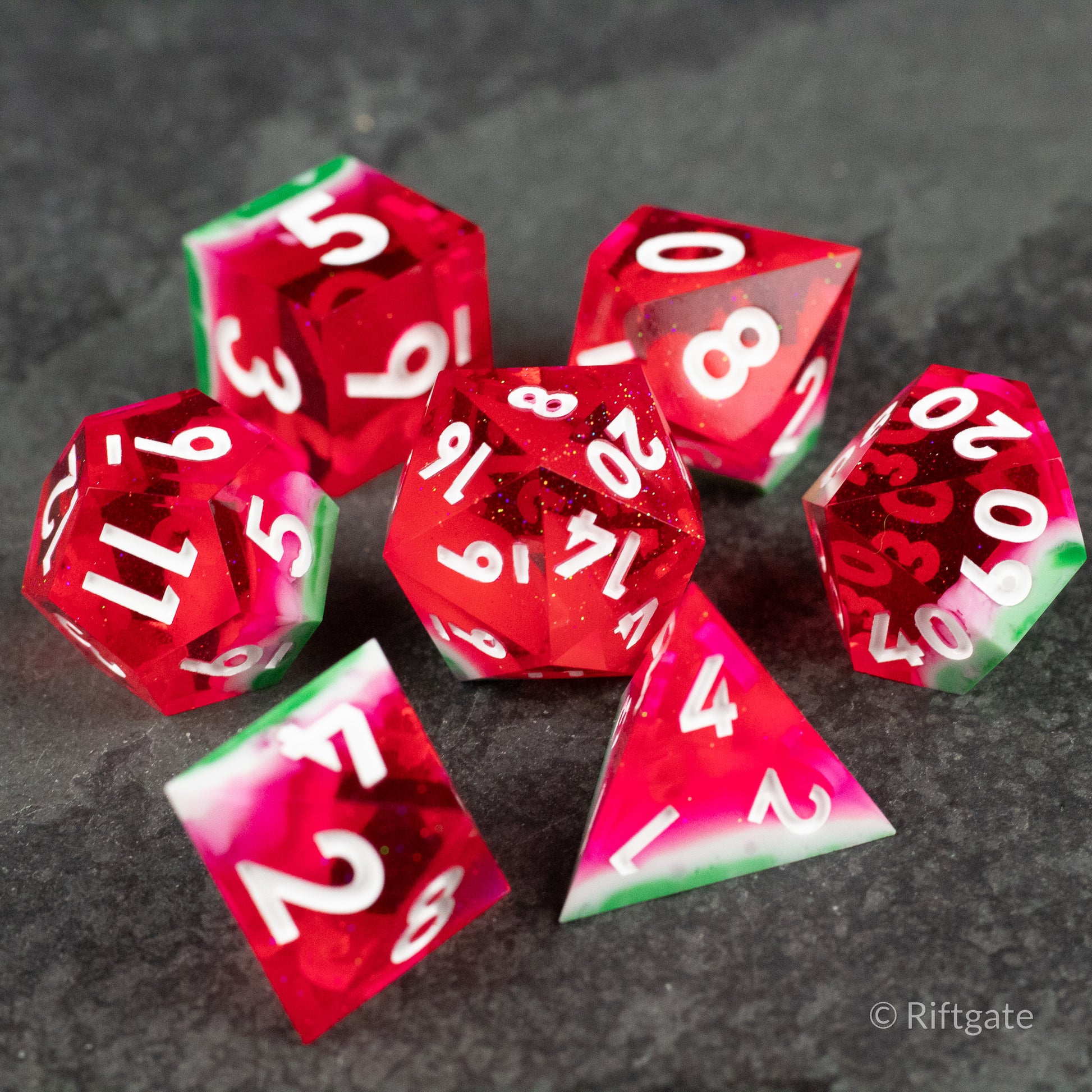 Watermelon Sharp Edge Dice - Set of seven sharp-edged polyhedral dice resembling watermelon slices, translucent red with green edges and white numbers.