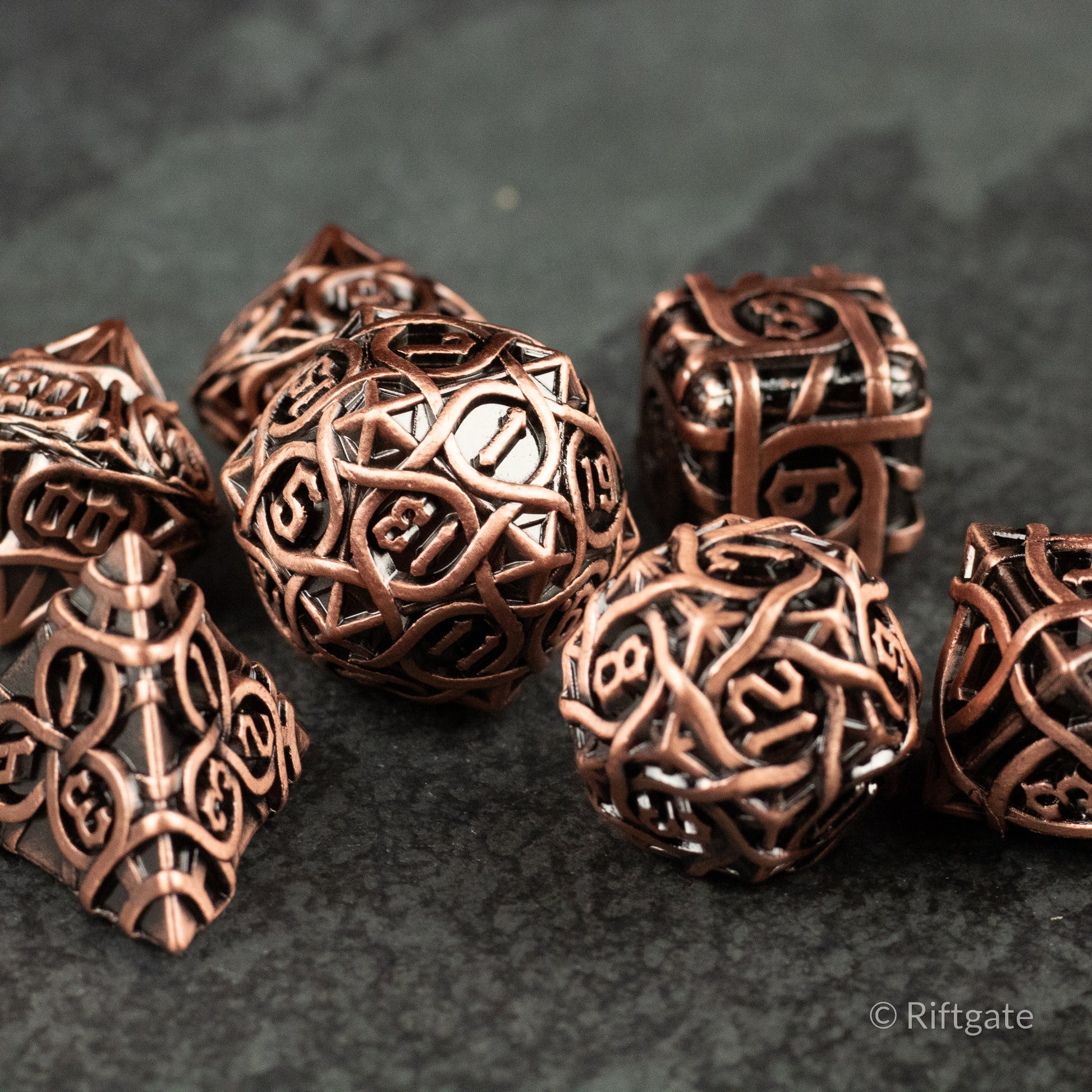 Runeweave Metal Dice Set - Copper-colored metal dice set with intricate rune-like engravings, featuring various polyhedral shapes.