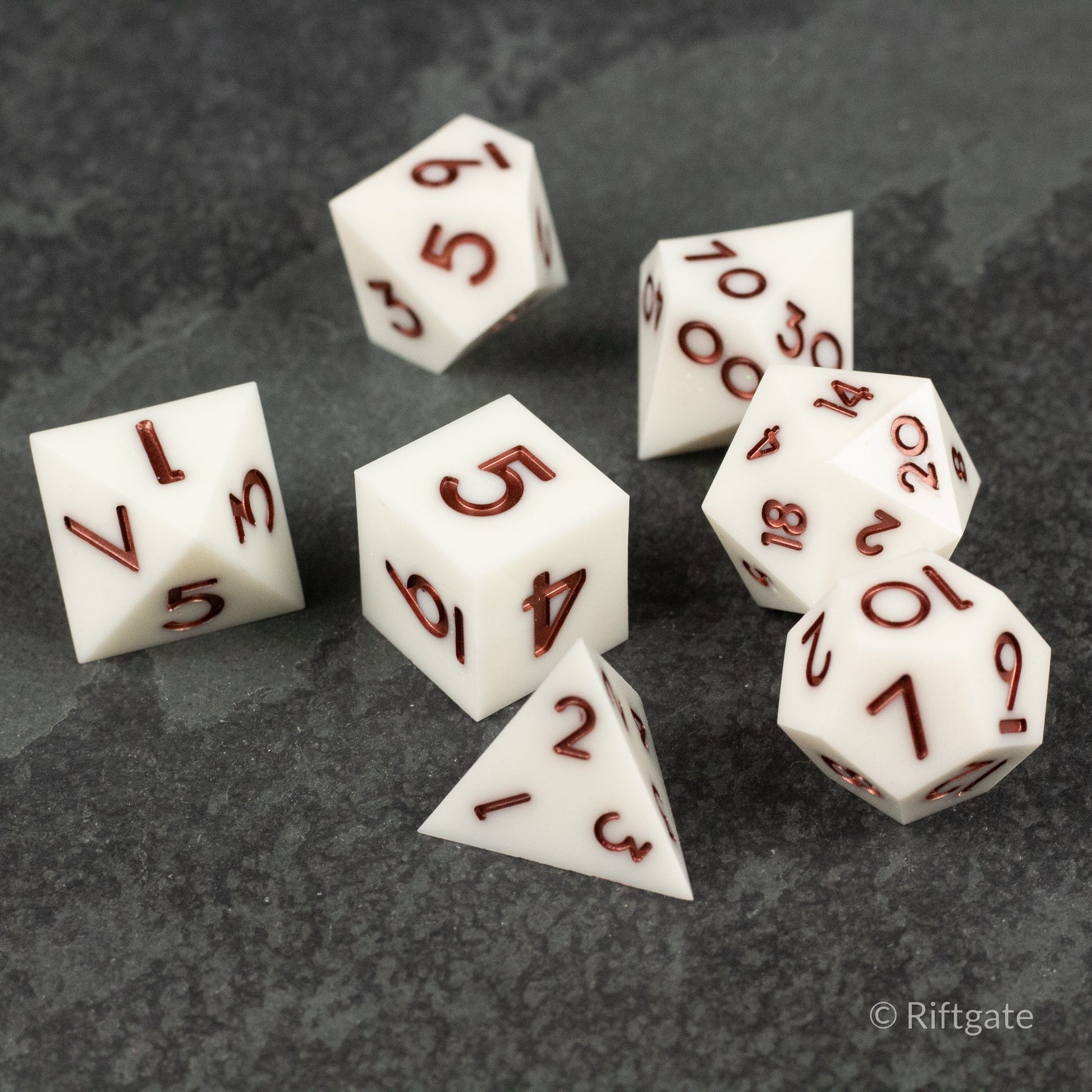 Glacial Spark Dice Set - Seven white polyhedral dice with sharp edges and deep red numbers on a dark textured surface.