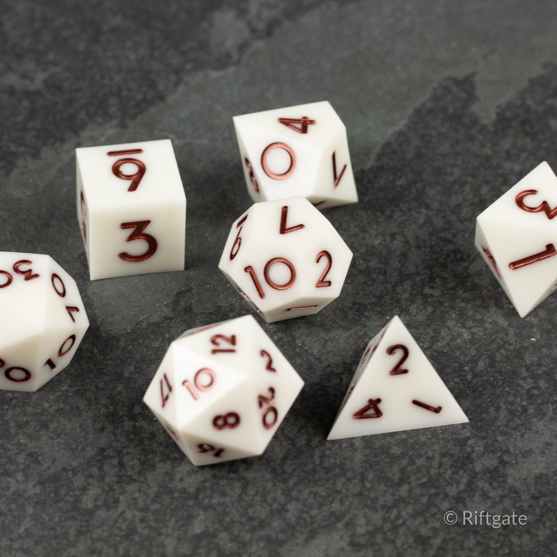 Glacial Spark Dice Set - White sharp-edged polyhedral dice set with red numbers on a dark textured surface.