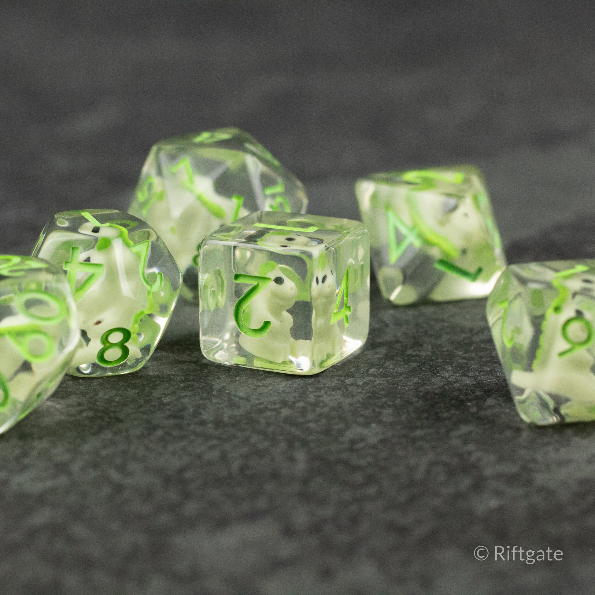 Green T-Rex Dice Set - Translucent green polyhedral dice with black numbers, including d20, d12, d8, d6, and d4 shapes on a dark textured surface.
