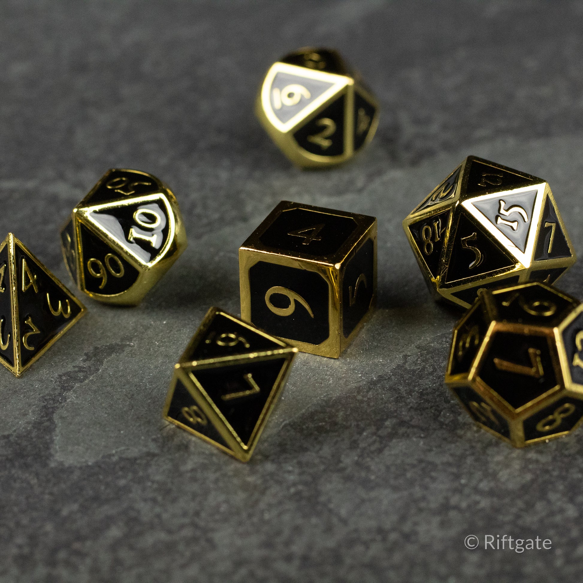 Aurum Eclipse Dice Set - Set of black metal polyhedral dice with gold numbers and edges, including d4, d6, d8, d10, d12, and d20 shapes on a dark.