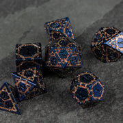 Gold Superior Ward Metal Dice Set - Black metal polyhedral dice set with gold intricate filigree patterns on dark stone surface.