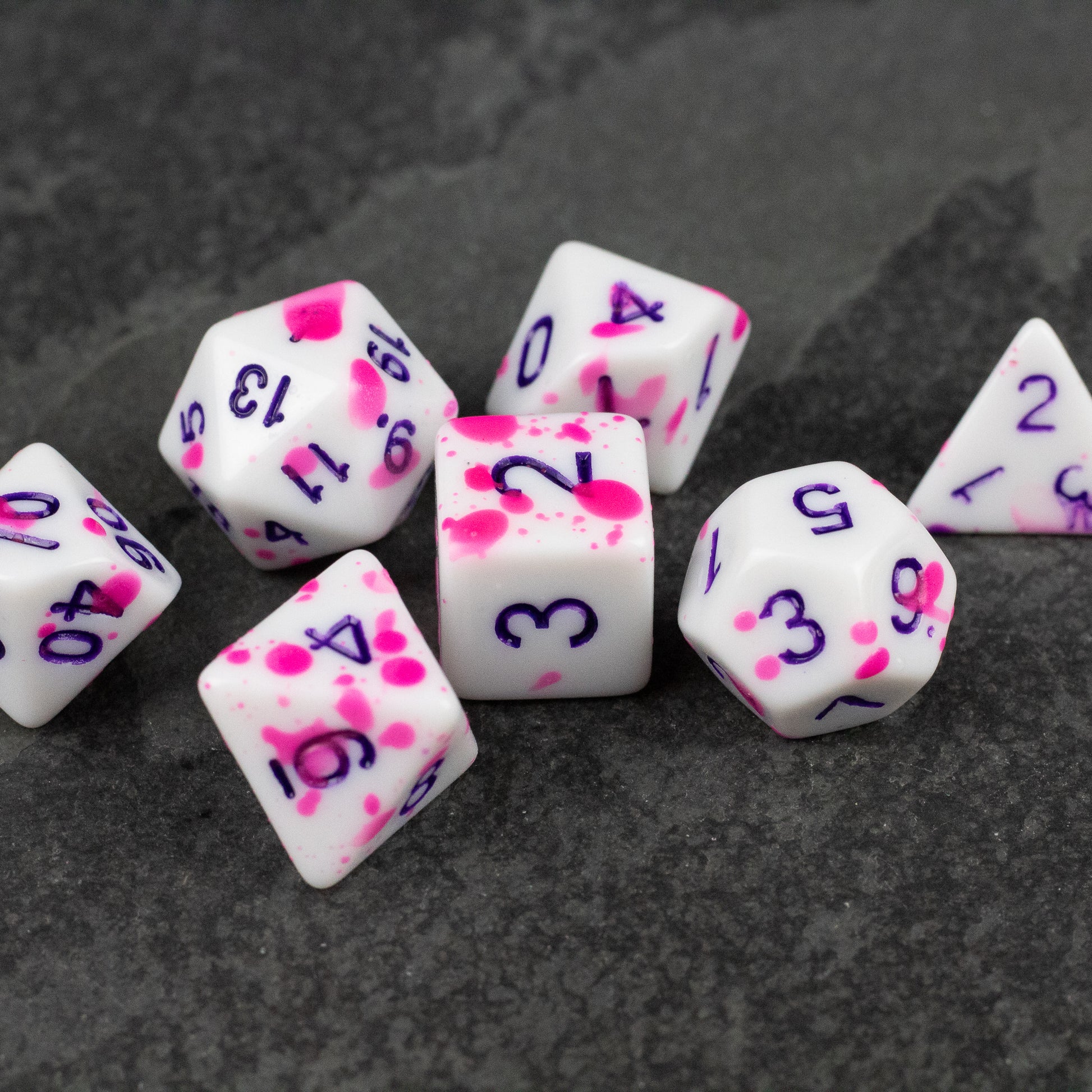 Color Change Purple Splatter Dice Set - White polyhedral dice set with purple numbers and vibrant pink splatter accents on each die.