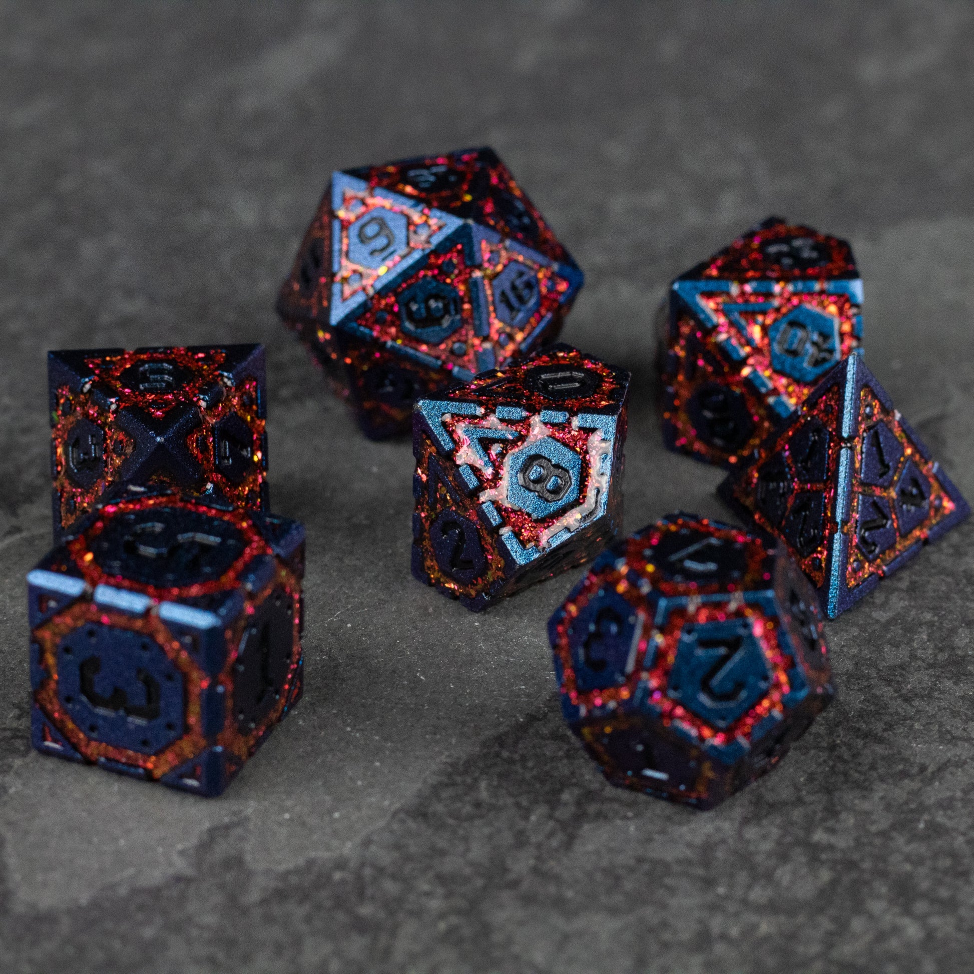 Red Superior Ward Metal Dice Set - Set of seven metal polyhedral dice in red with black speckles and blue recessed numbers.