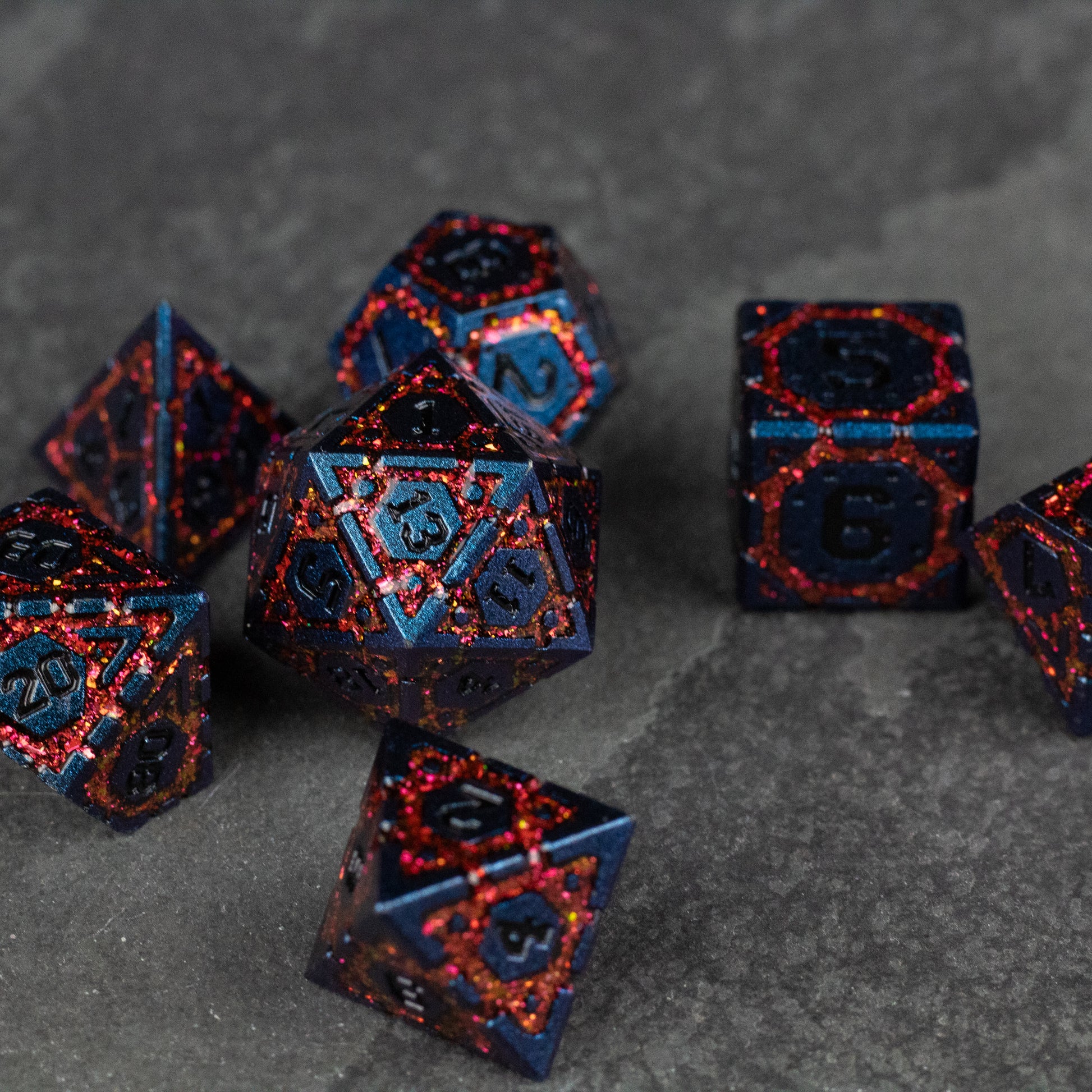 Red Superior Ward Metal Dice Set - Set of seven red and black metal polyhedral dice with intricate angular pattern and blue numbers on gray surface.