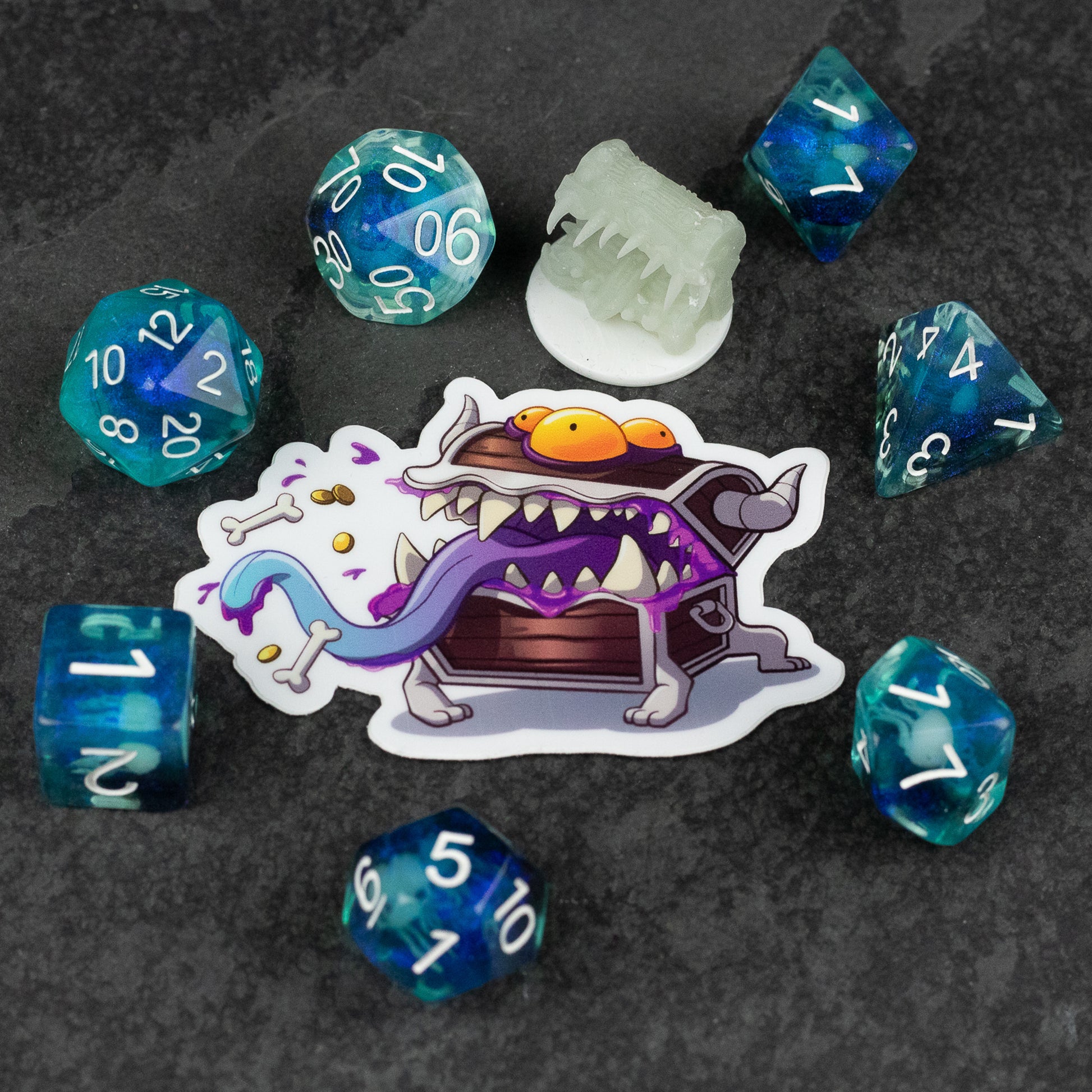 Dice Club - Set of seven blue and teal polyhedral dice with white numbers surrounding a cartoon monster sticker with orange eyes and.