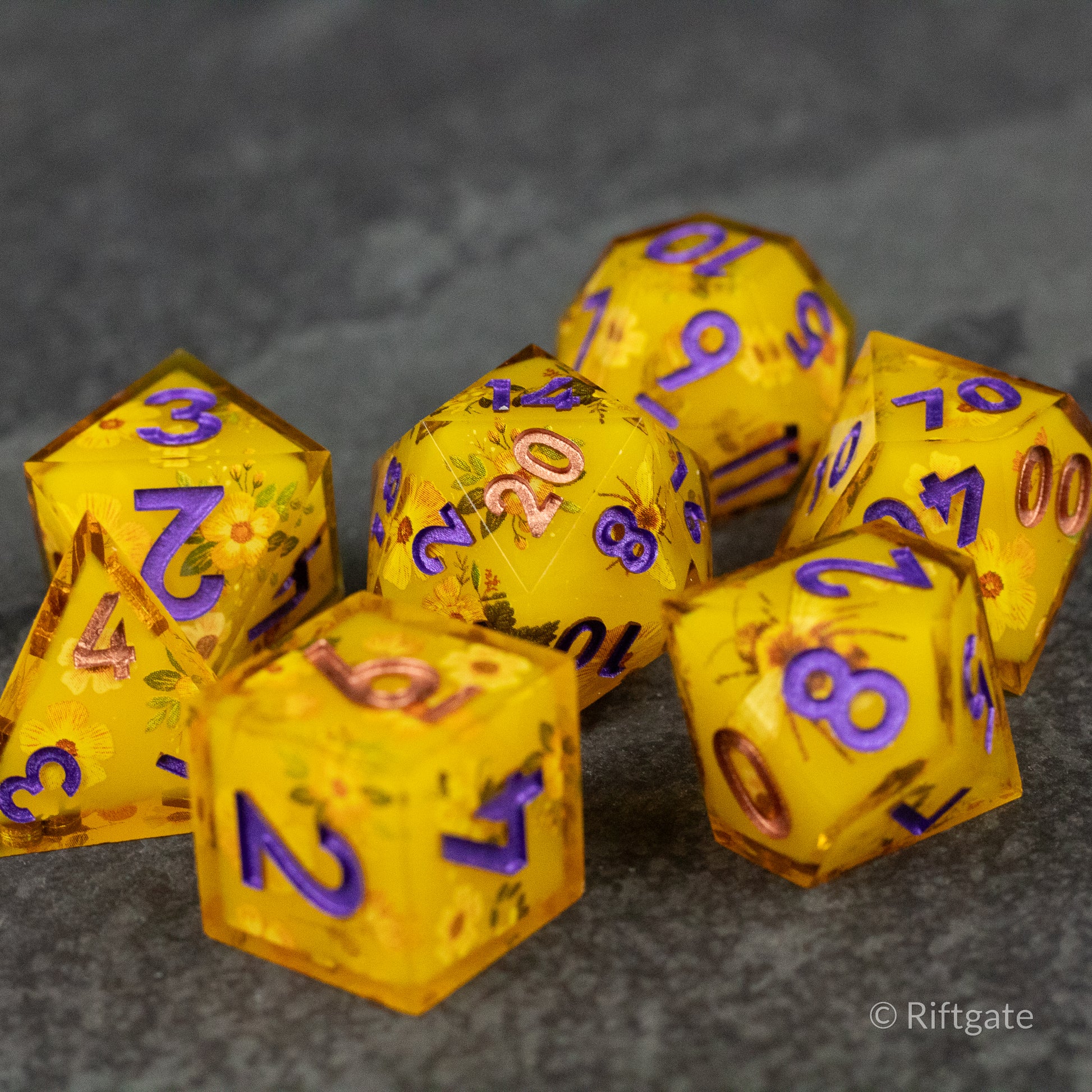 Honey Bees and Flowers Sharp Edge Dice - Seven sharp edge dice set in translucent golden yellow with embedded honey bee and flower designs, purple numbering.