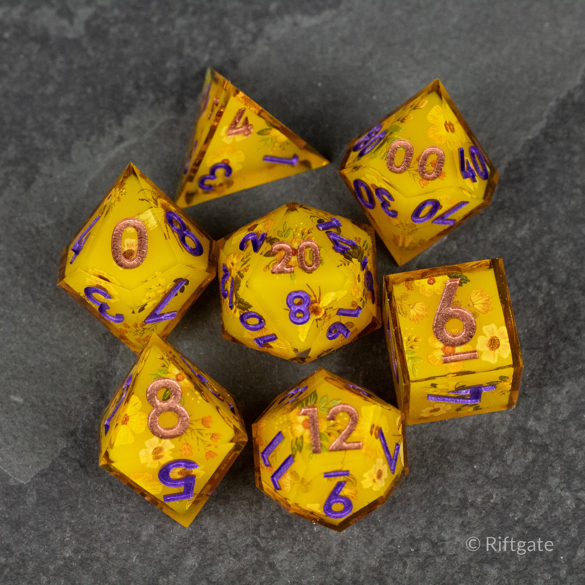 Honey Bees and Flowers Sharp Edge Dice - Set of seven translucent golden-yellow sharp edge dice with embedded honey bee and flower designs, purple numerals visible.