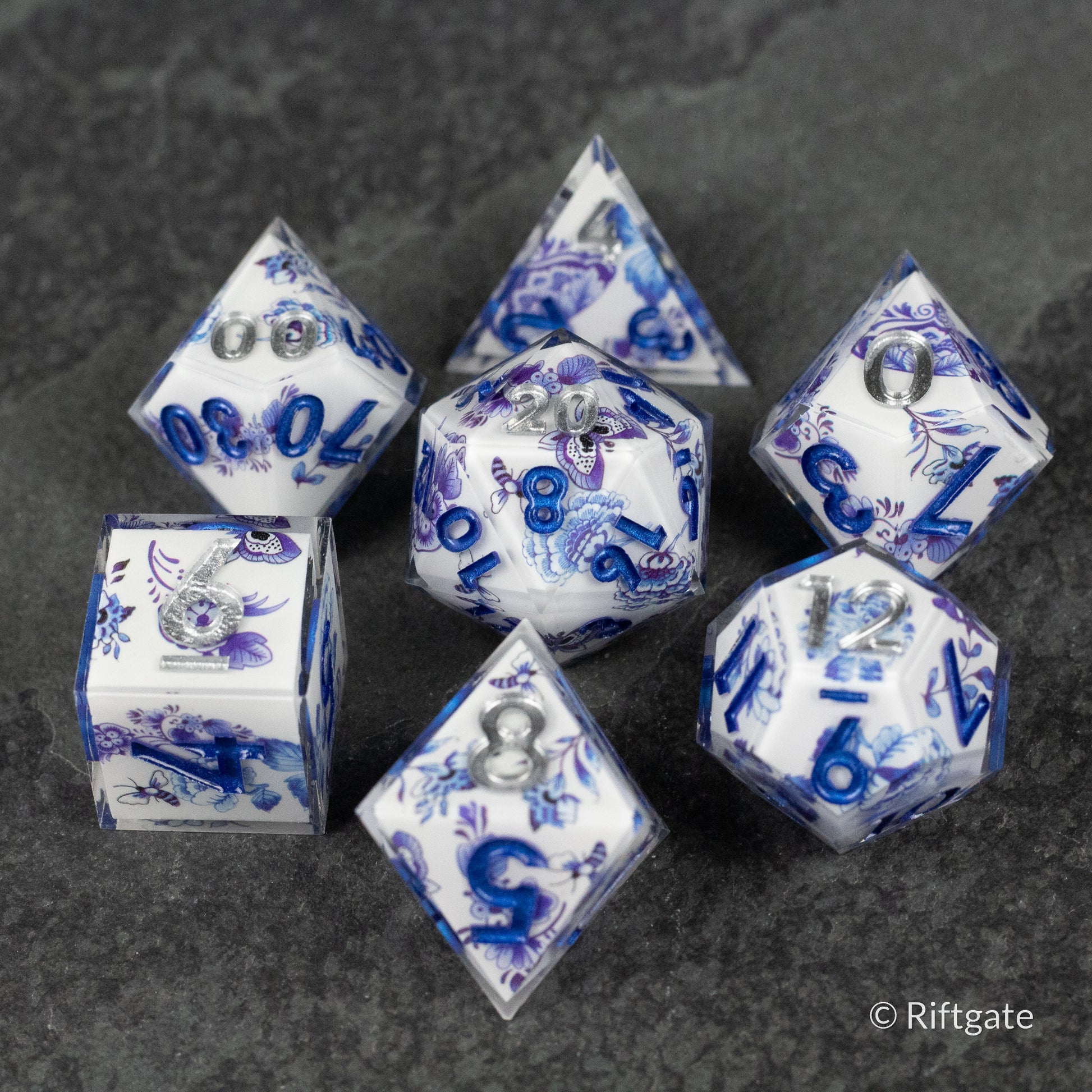 Moonlight Garden Dice Set - Set of seven translucent white polyhedral dice with intricate blue floral and moon designs and dark blue numbers.