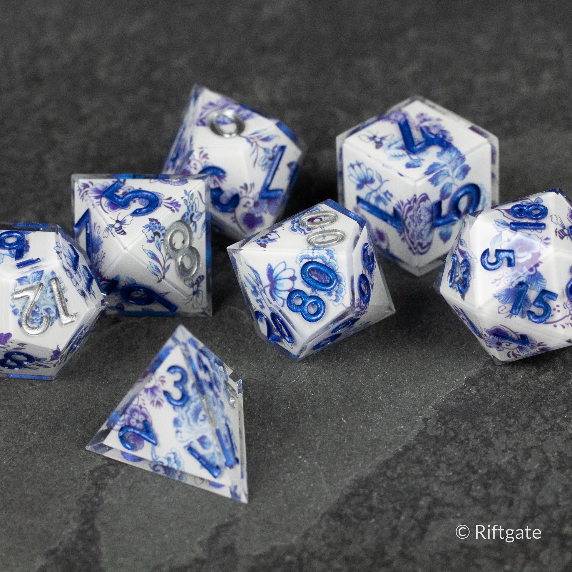 Moonlight Garden Dice Set - Translucent white polyhedral dice set with swirling blue patterns and bold blue numbers on dark gray surface.
