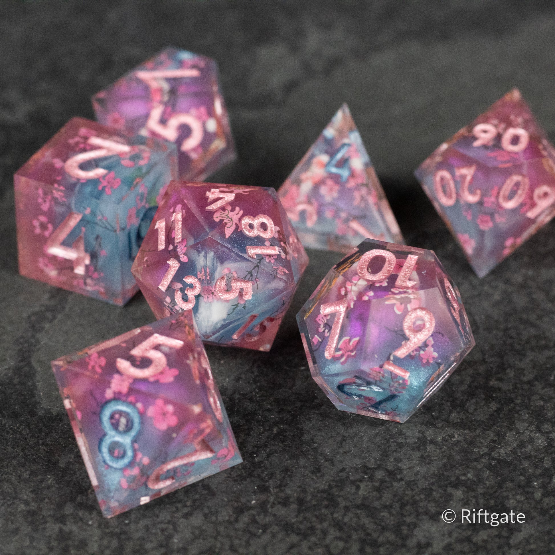 Twilight Blossoms Dice Set - Set of seven transparent pink and blue sharp-edged polyhedral dice with white numbers, designed for tabletop gaming.