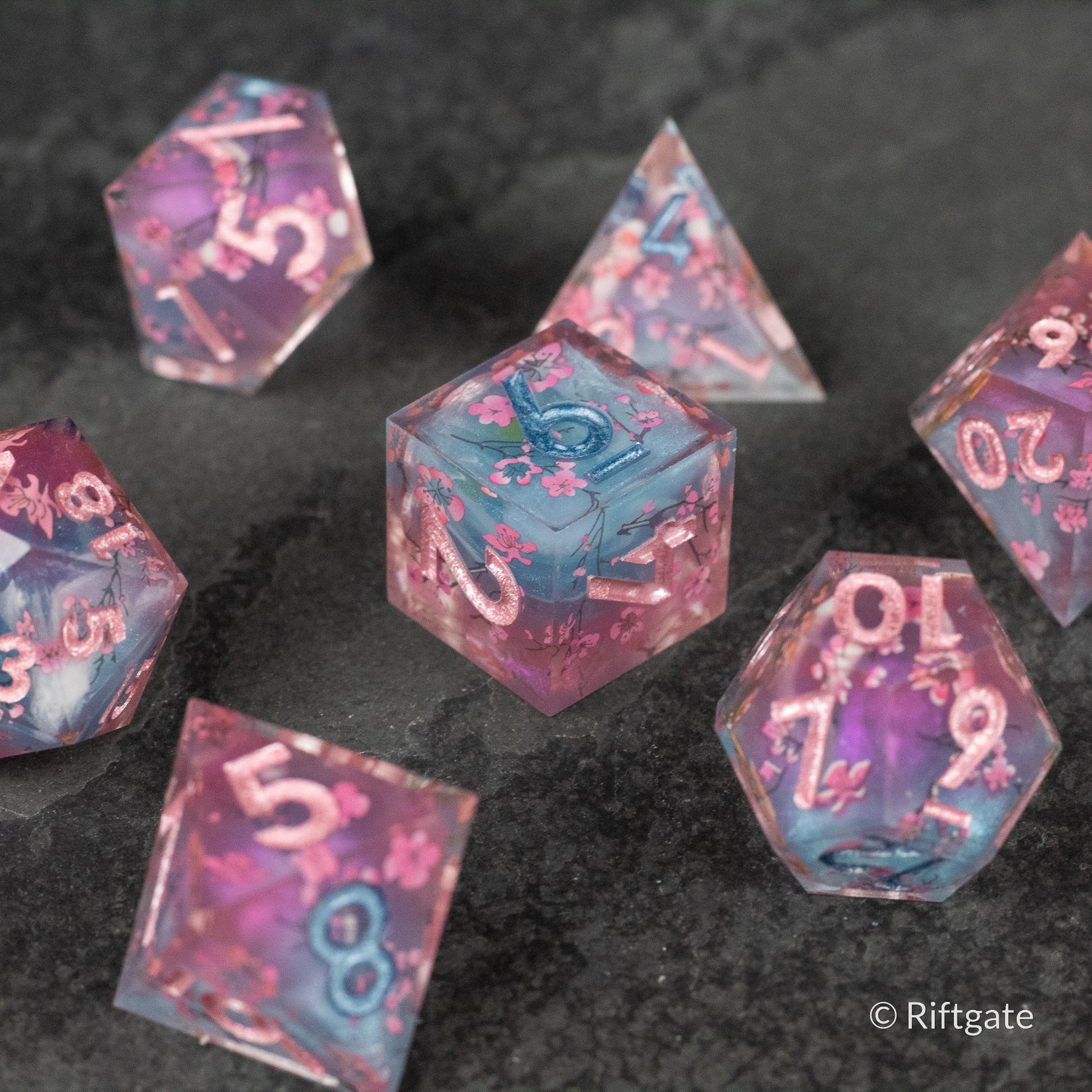 Twilight Blossoms Dice Set - Transparent purple polyhedral dice with pink and blue floral inclusions and sharp edges, featuring white numbering.