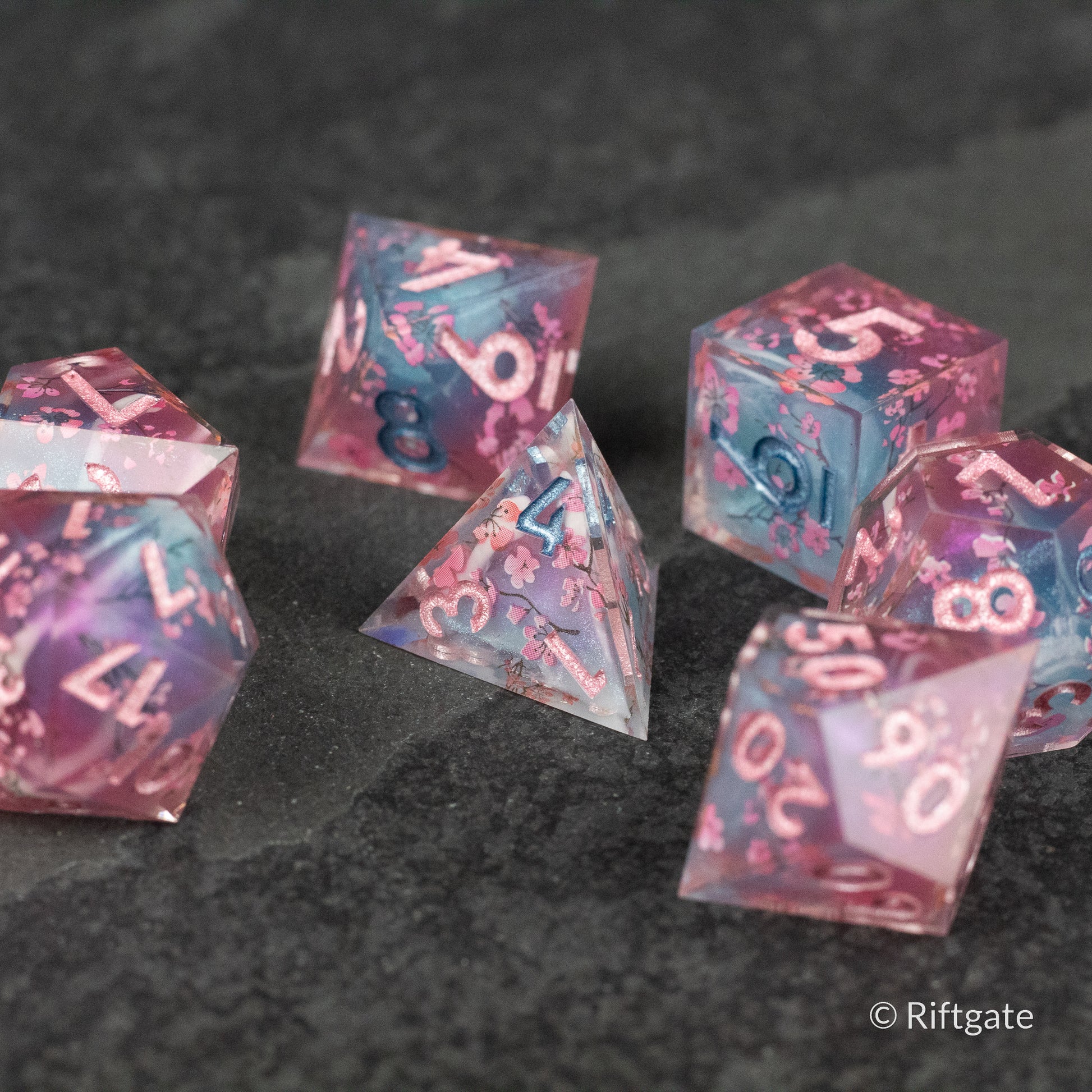 Twilight Blossoms Dice Set - Translucent purple and pink sharp-edged polyhedral dice set with white and blue numbers.